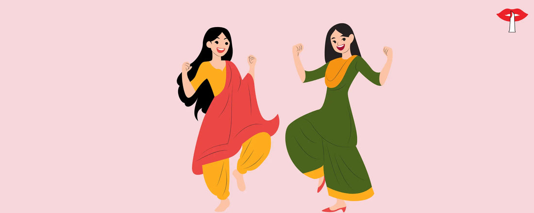 Two women in vibrant red and green indian traditional outfits dancing joyfully in the comfort of Gossip Lingerie