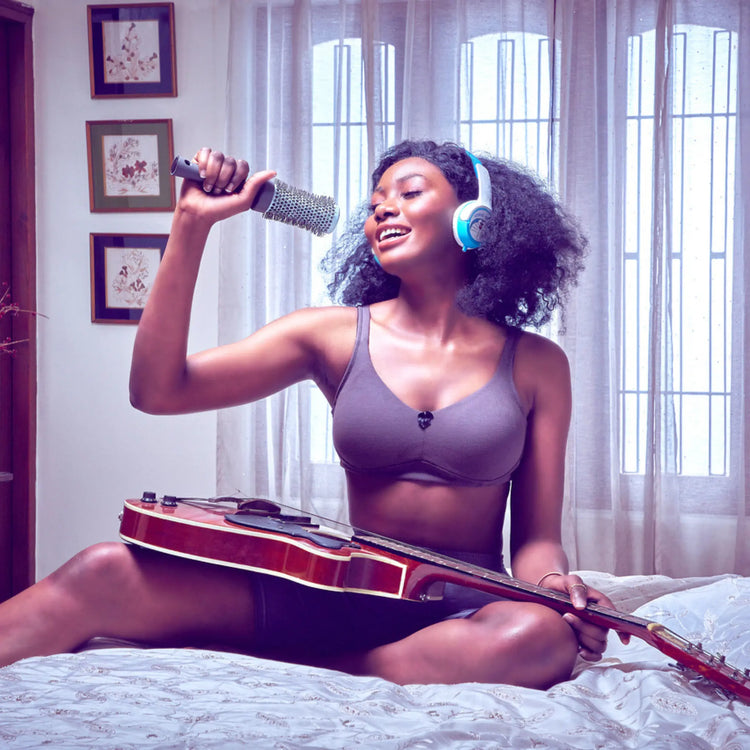 Woman relaxing indoors wearing an everyday bra while singing and enjoying music, showcasing the comfort and ease of the everyday bra